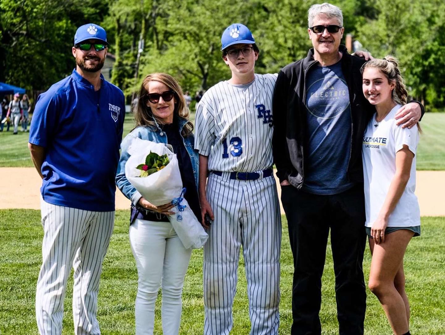 Theo in a baseball uniform with family and coach