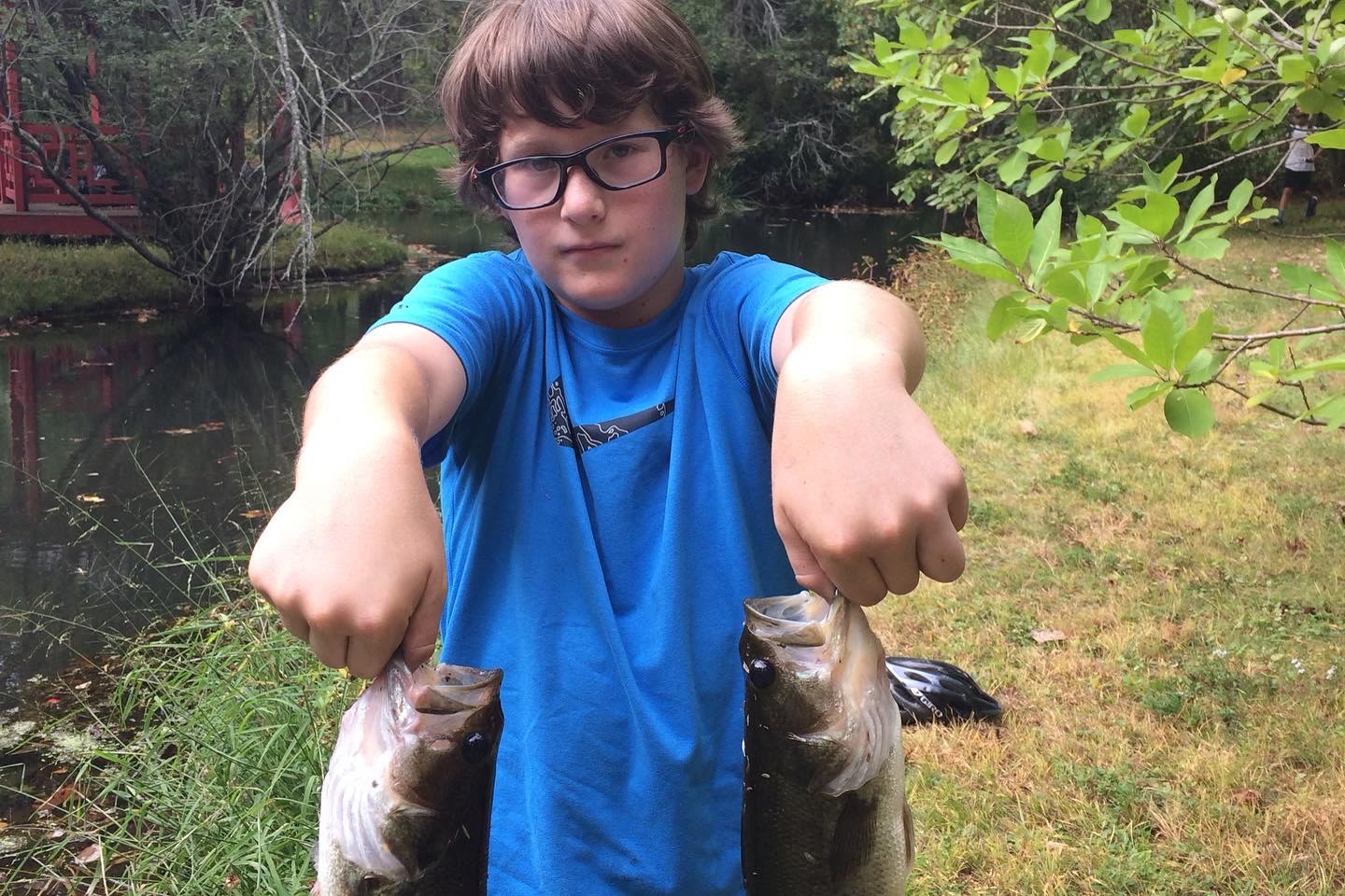 Theo holding two fish by a pond